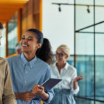 two young cheerful diverse colleagues talking after business meeting while standing in the modern office or coworking space